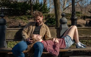 Couple relaxing on a Central Park bench, woman lying across man's lap in a candid outdoor moment.