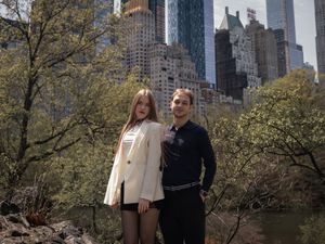 Couple posing together on rocky terrain in Central Park with Manhattan skyscrapers in the background.