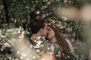 Romantic couple sharing a tender kiss surrounded by blooming white flowers and lush green foliage.
