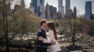 Couple embracing near Central Park with NYC skyline and Wollman Rink visible in the background.