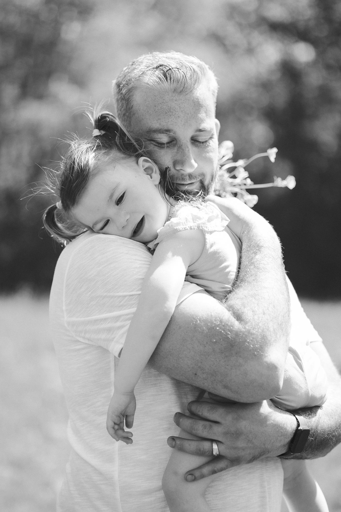 An engaged couple holds each other, the man's arm is around the woman's shoulder as they both look into the distance.