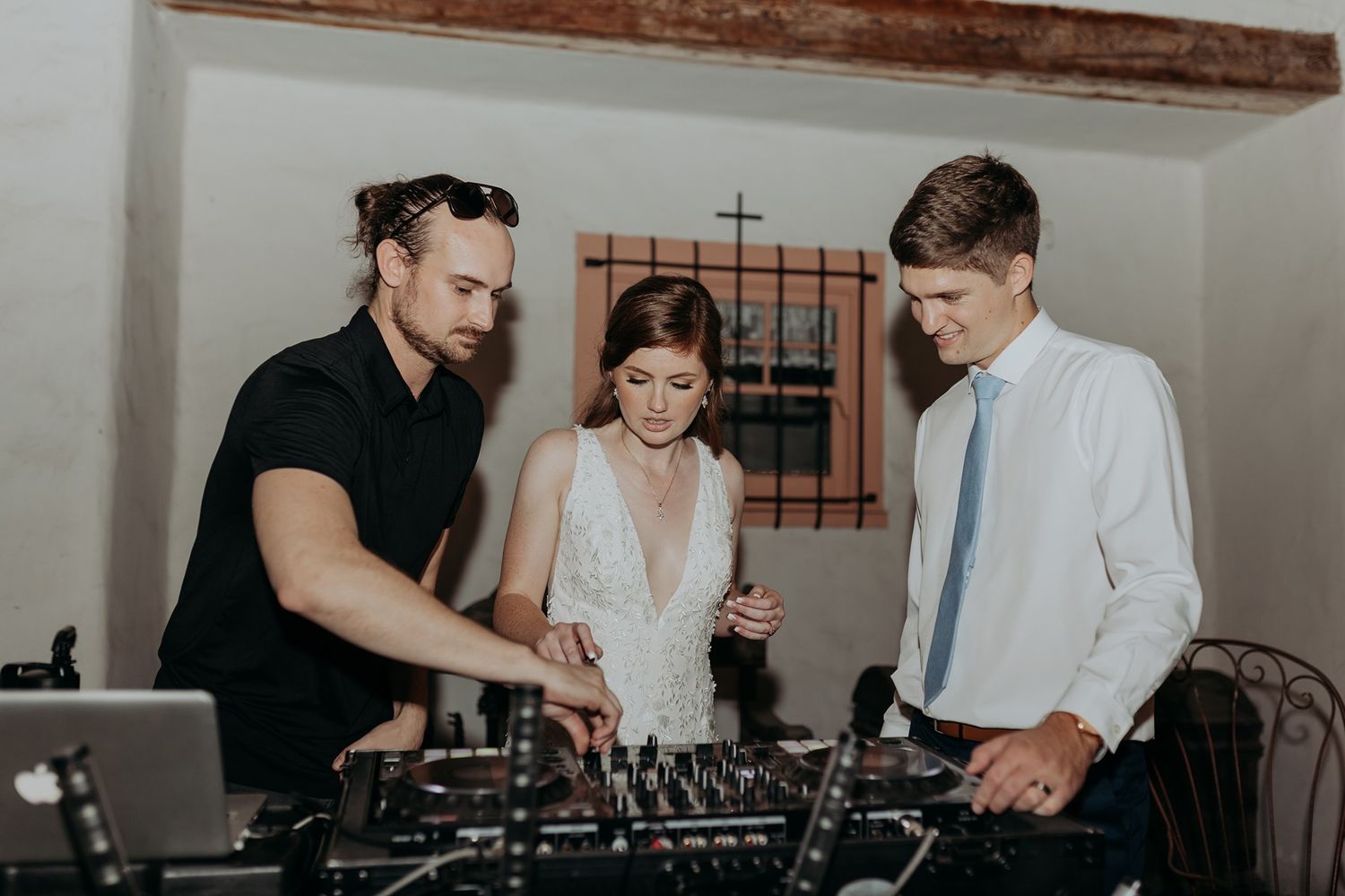 Bride and groom learning to DJ at wedding reception with professional DJ at mixing equipment at Rancho Buena Vista Adobe.