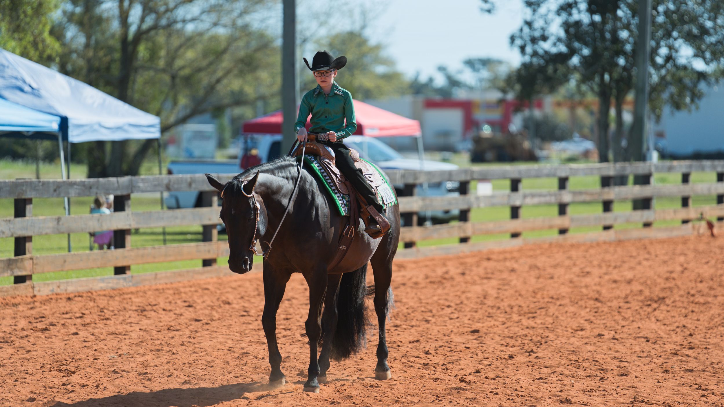 A horse and rider walk across a red clay arena during an equestrian training session.
