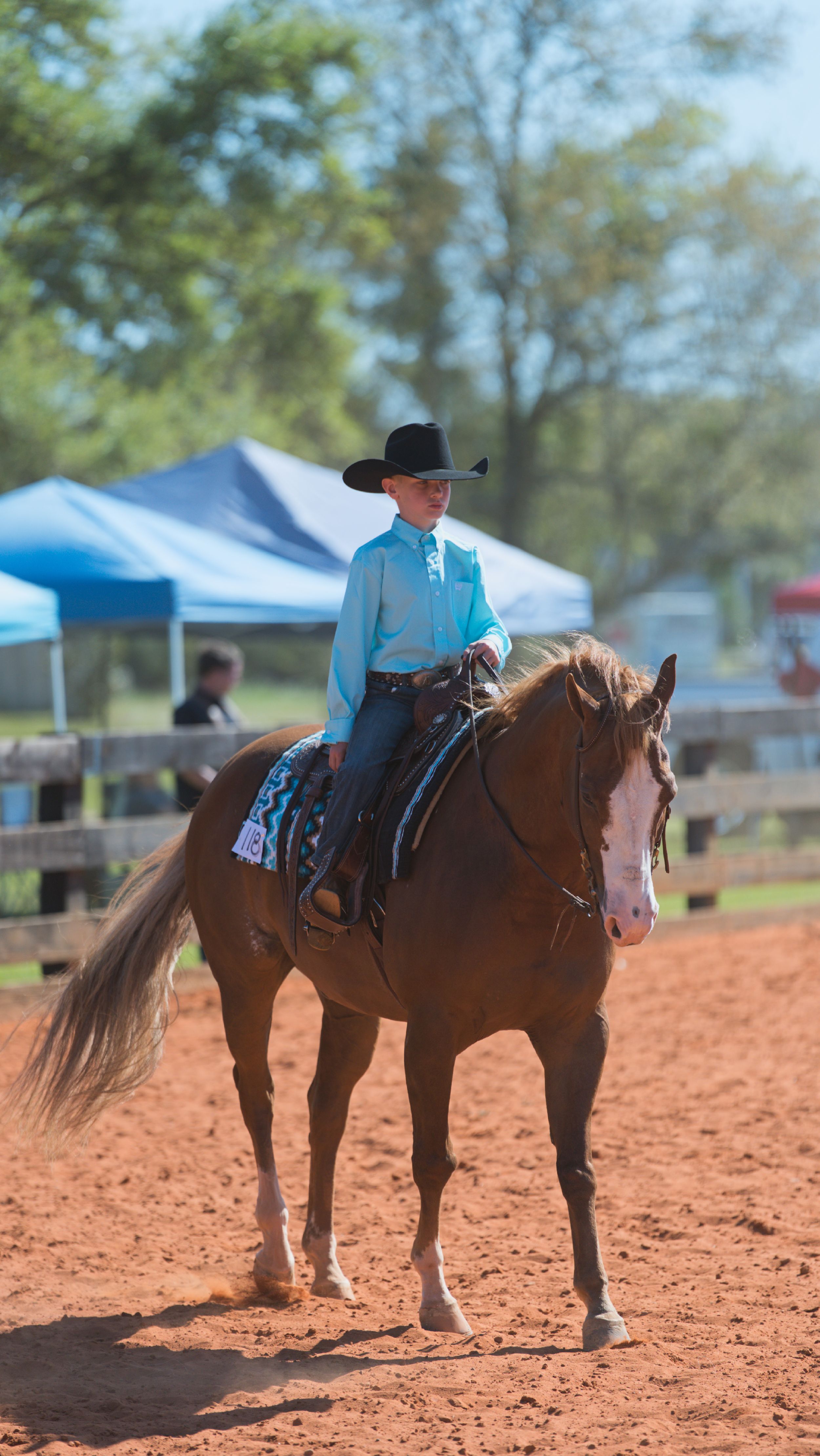 Riders on horseback line up in a row on red dirt arena ground during an equestrian event.