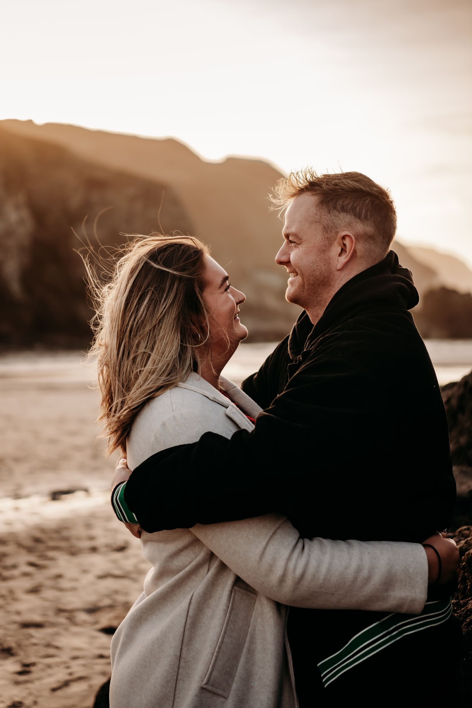 A couple embraces lovingly on a beach at sunset, creating a romantic silhouette against the golden sky.