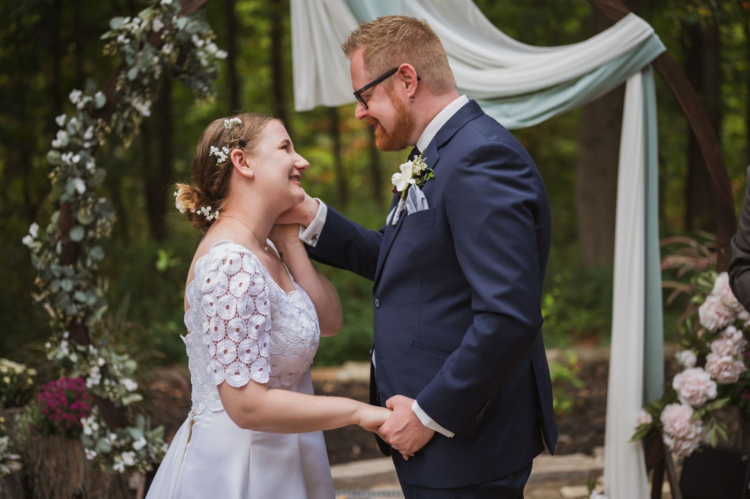 A couple shares joyful embraces outdoors in wedding attire with natural sunlit greenery in the background.