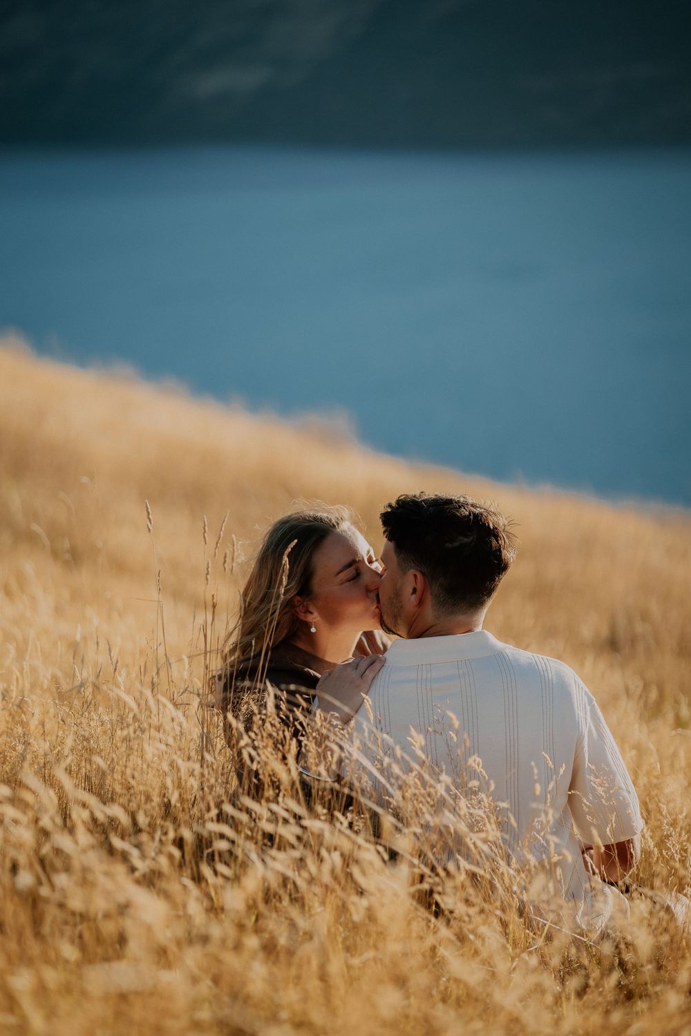A romantic couple lies together in a golden wheat field under a blue summer sky.