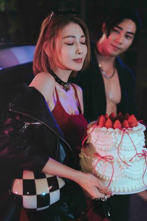 A beautifully decorated white cake topped with fresh strawberries is being held at a dimly lit celebration.在燈光昏暗的慶祝活動中，擺放著一個裝飾精美的白色蛋糕