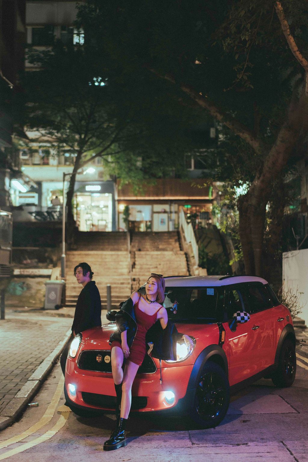 A group of people pose around a red sports car at night on a dimly lit street.夜幕降臨，一群人圍著一輛紅色跑車在昏暗的街道上擺姿勢拍照。