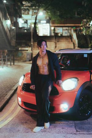 A person poses next to a sleek red sports car at night, illuminated by street lights and headlights夜幕降臨，路燈和車燈照亮了一輛線條流暢的紅色跑車，獨自站在車旁擺姿勢拍照。