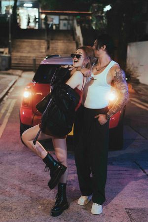 Two people in casual attire dance together on a city street at night with car headlights glowing in the background.夜幕降臨，兩名身著便服的人在城市街道上翩翩起舞
