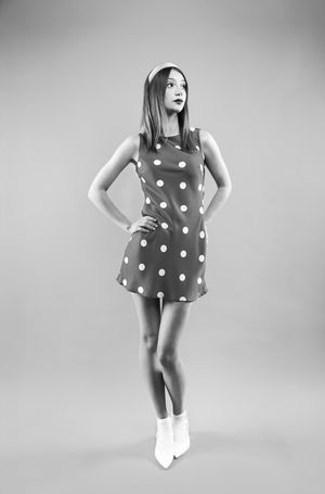 Girl in a red polka dot dress with red dots, a pink headband with hands on hips, looking right, black and white image