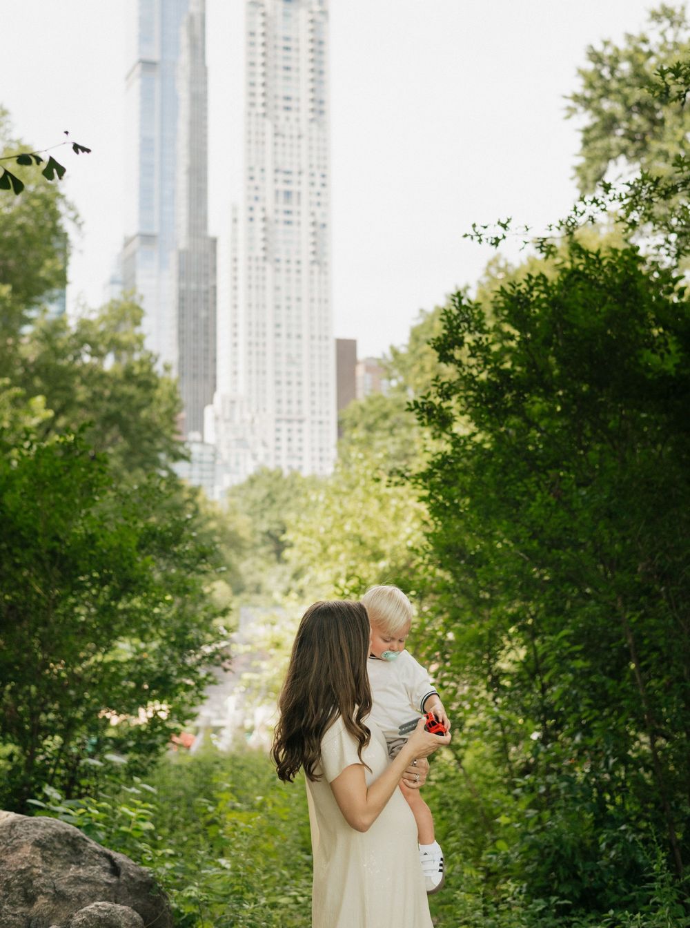 A parent and baby share a tender moment in Central Park with Manhattan skyscrapers rising in the background.