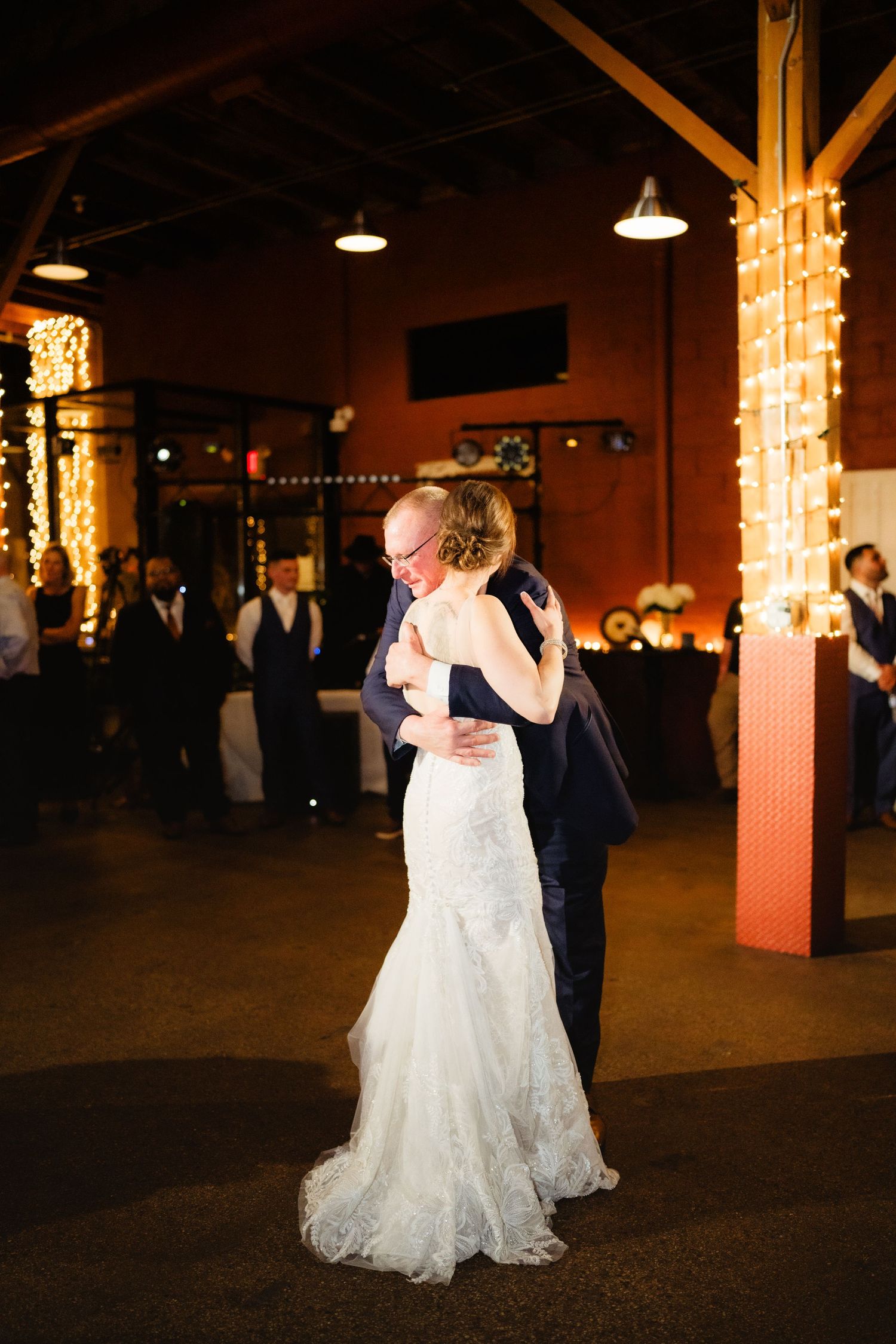 Bride and groom share their first dance in a warmly lit wedding reception venue decorated with string lights.