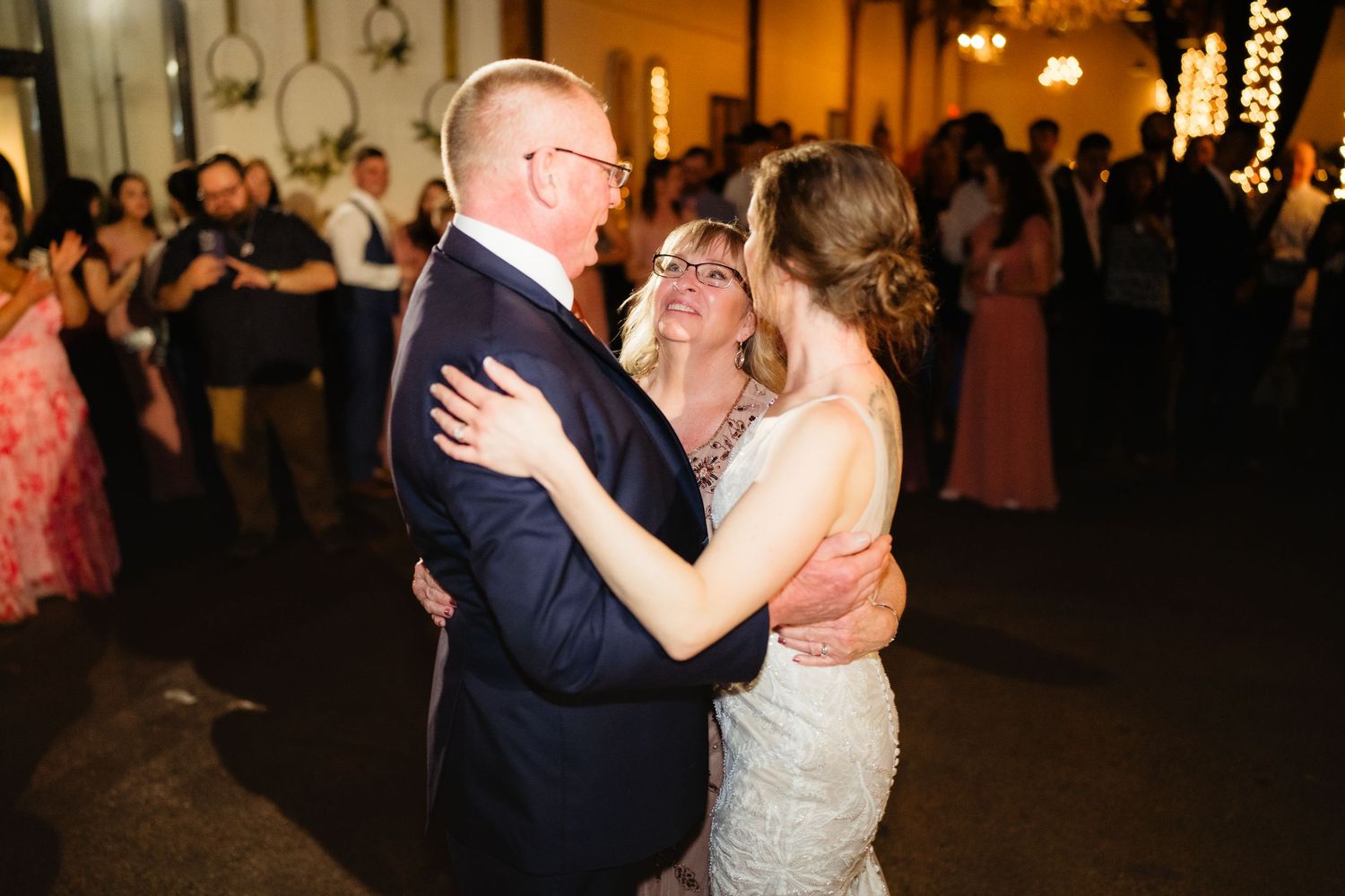 Bride and groom share a tender three-way dance with a family member at their wedding reception.