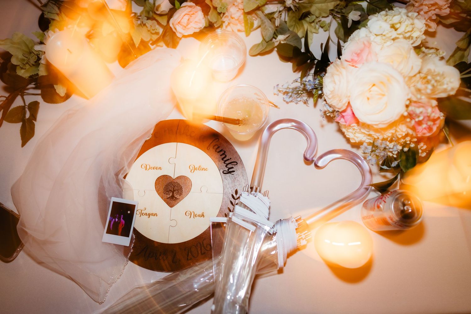Romantic wedding flat lay with floral arrangement, heart balloon, engraved wooden keepsake, and candles in warm light.