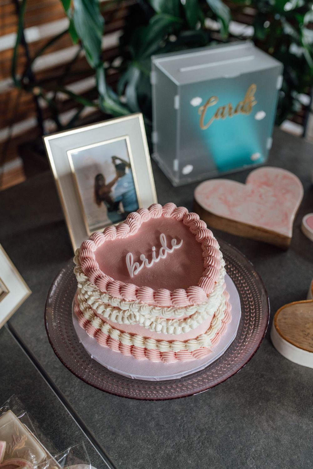 Heart-shaped pink bride cake with ruffled frosting displayed on a dessert table at a bridal shower.