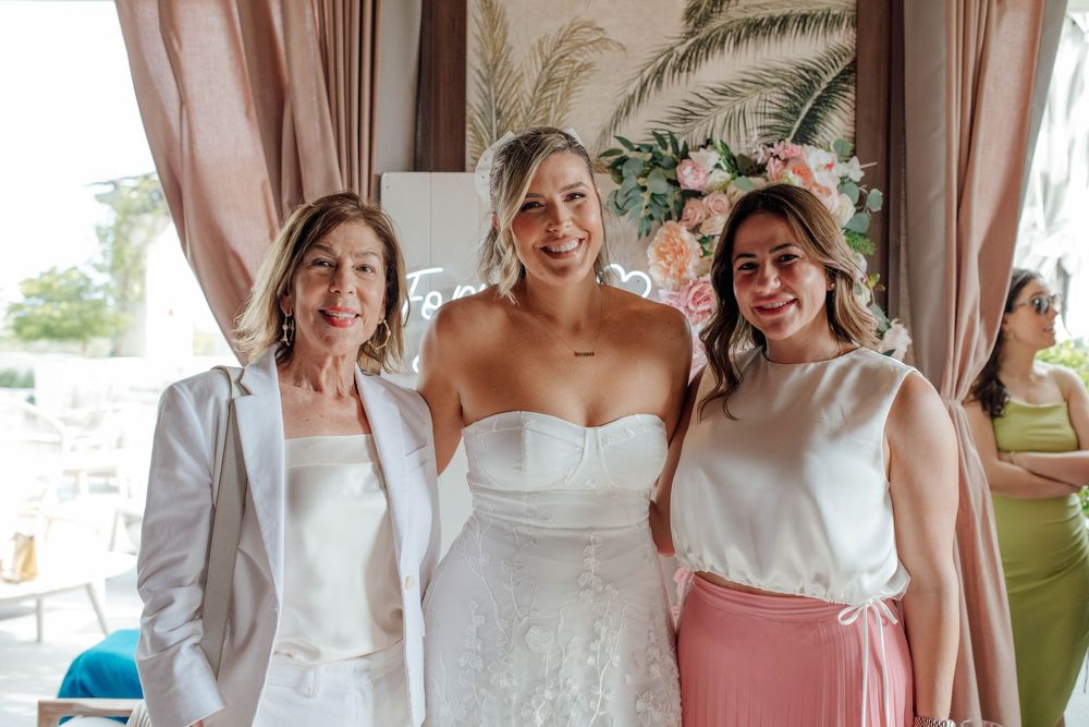Bride in strapless white wedding gown poses with two smiling women at elegant bridal shower event.
