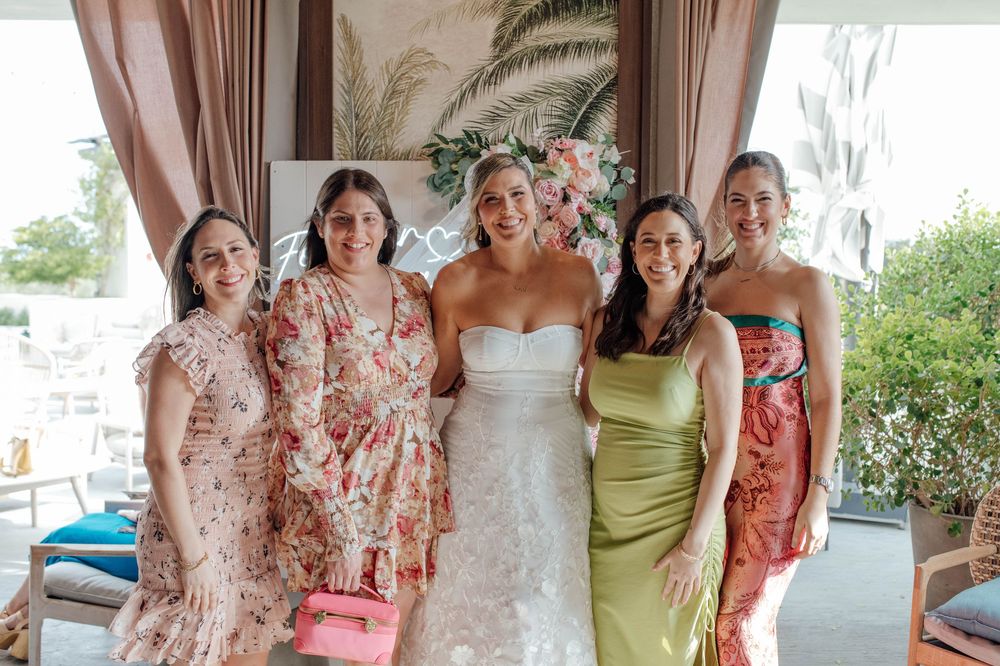 Bride in white strapless gown posing with four guests in colorful dresses at wedding celebration.