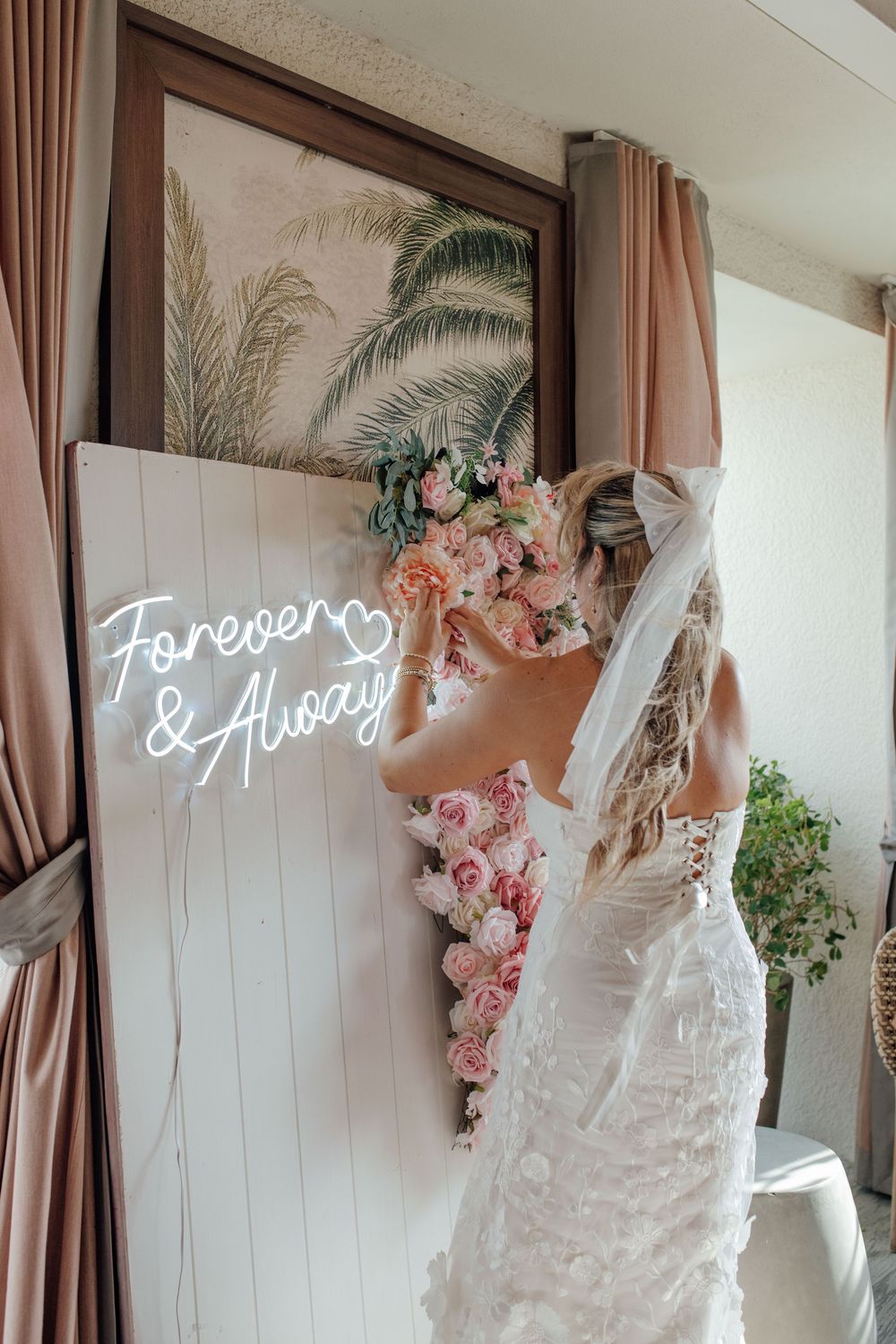 Bride arranges pink flowers on a white board with a Forever and Always neon sign.