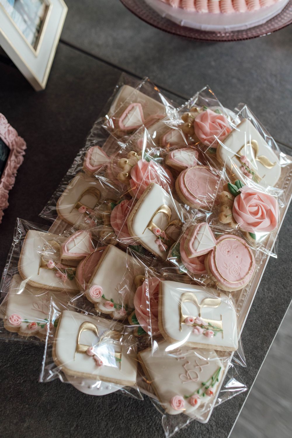 Elegant pink and white decorated bridal shower cookies wrapped in cellophane bags on a display tray.