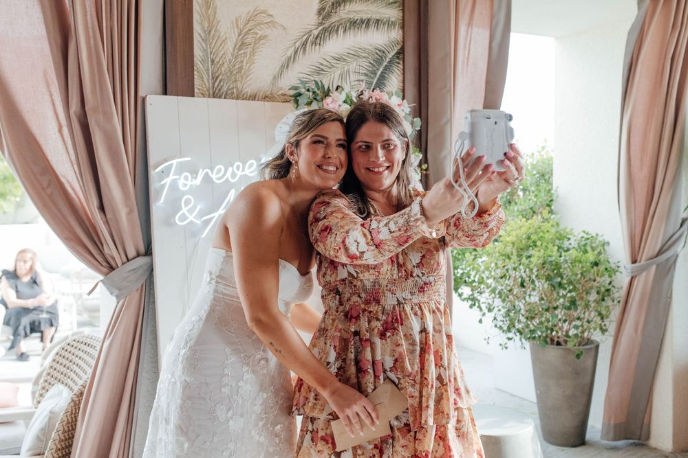 Bride and guest taking a selfie in front of a Forever & Always neon sign at a wedding reception.