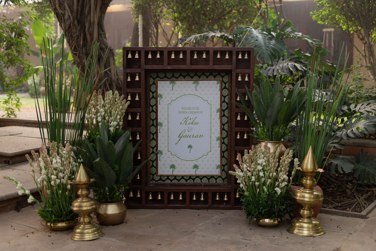 Outdoor wedding venue setup with gold vases, greenery, and wooden lattice fence creating an elegant garden atmosphere.