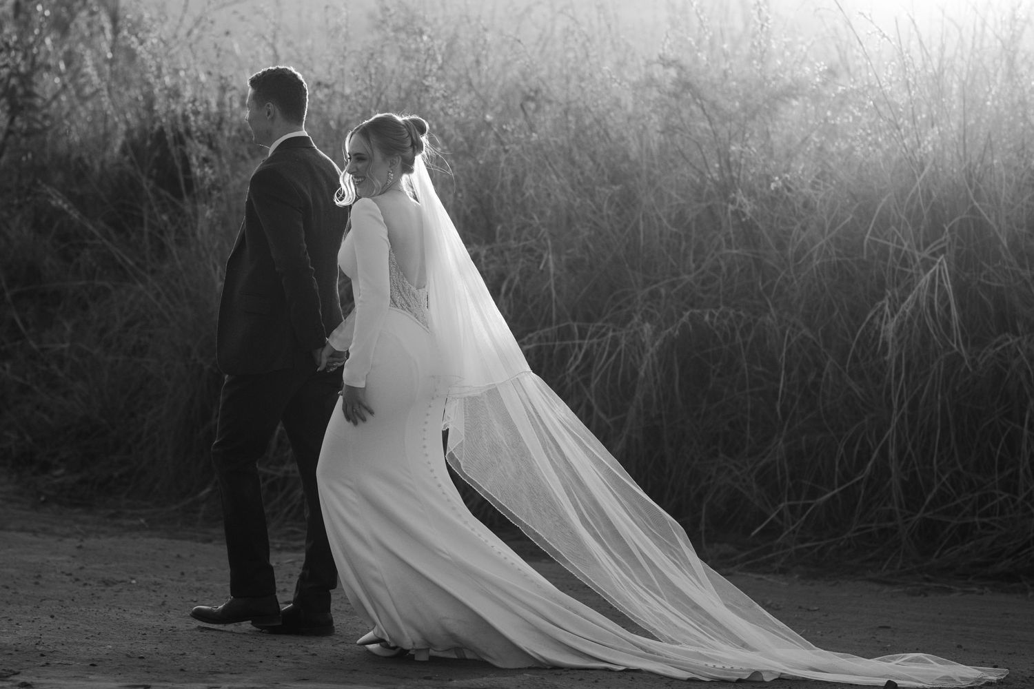 Black and white wedding photo of a couple walking together, bride in a long veil and gown.