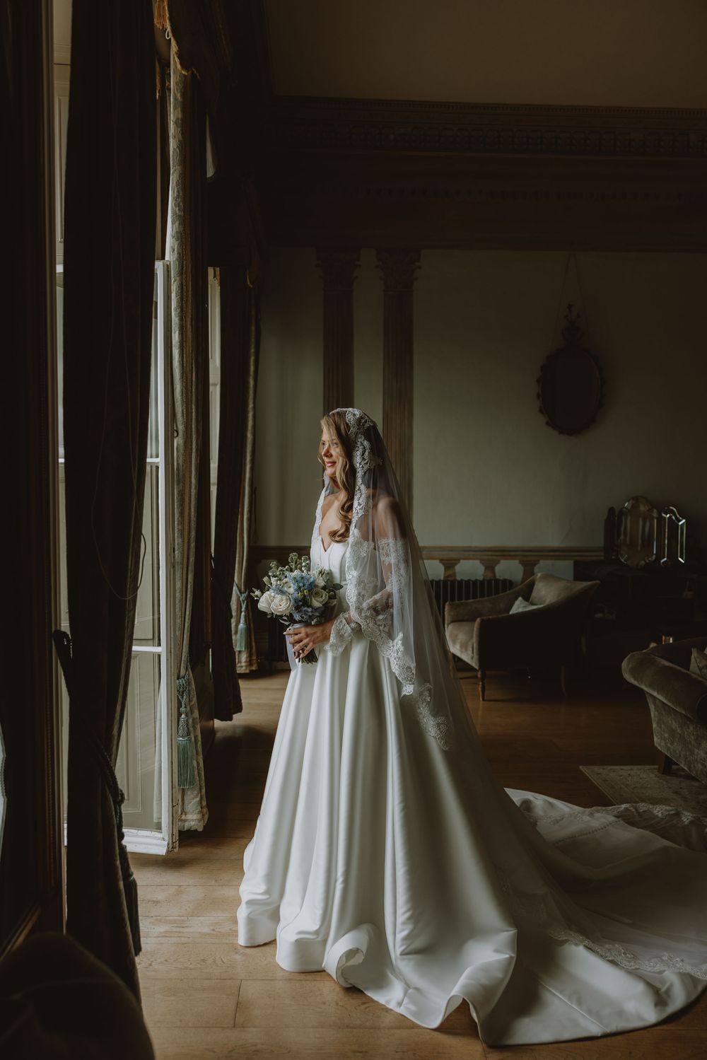 Moody artistic wedding photos show a bride in a flowing white gown and veil in a dimly lit vintage room.