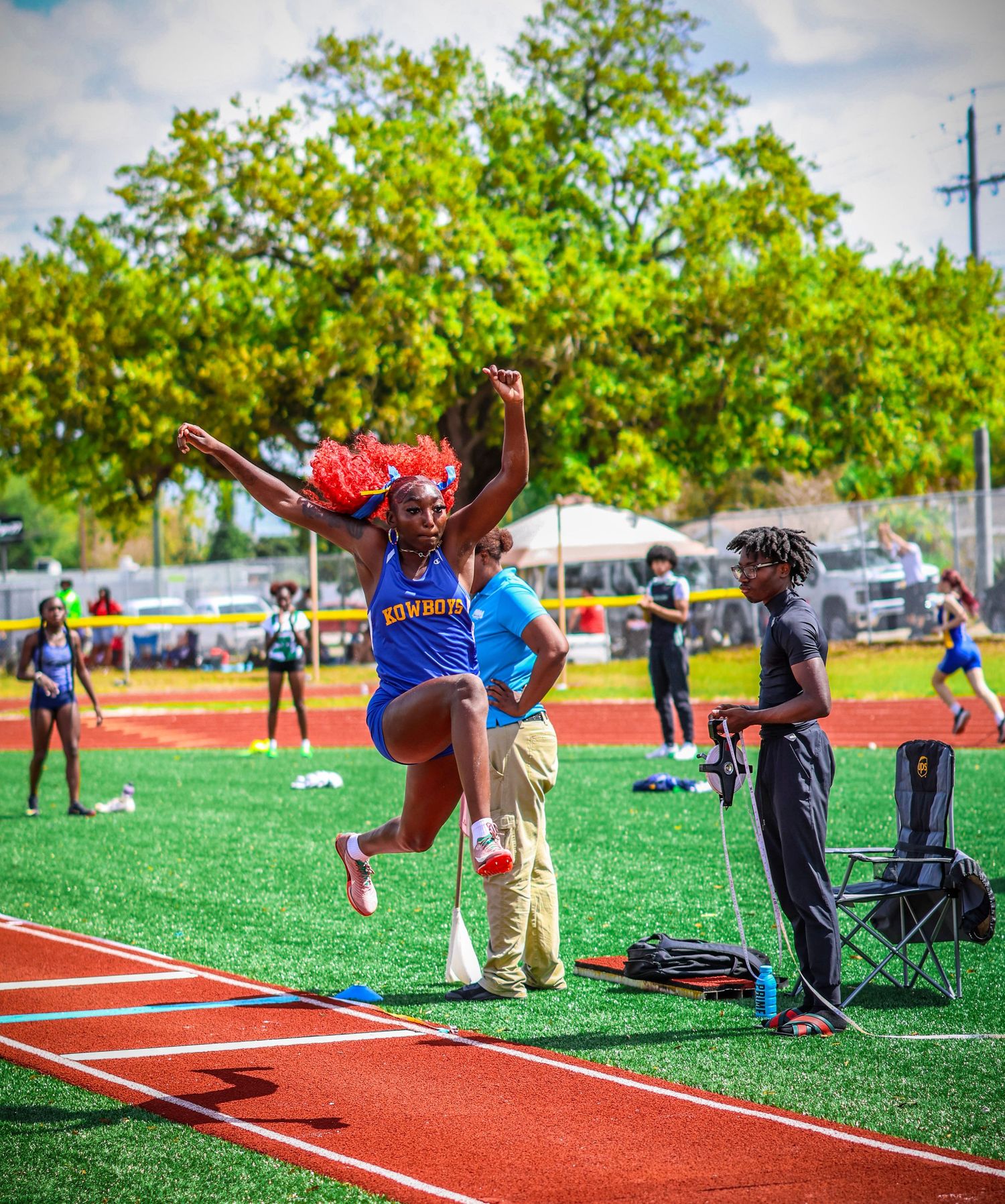 Athletes practicing long jump techniques on a red track with coaches observing their form during training.