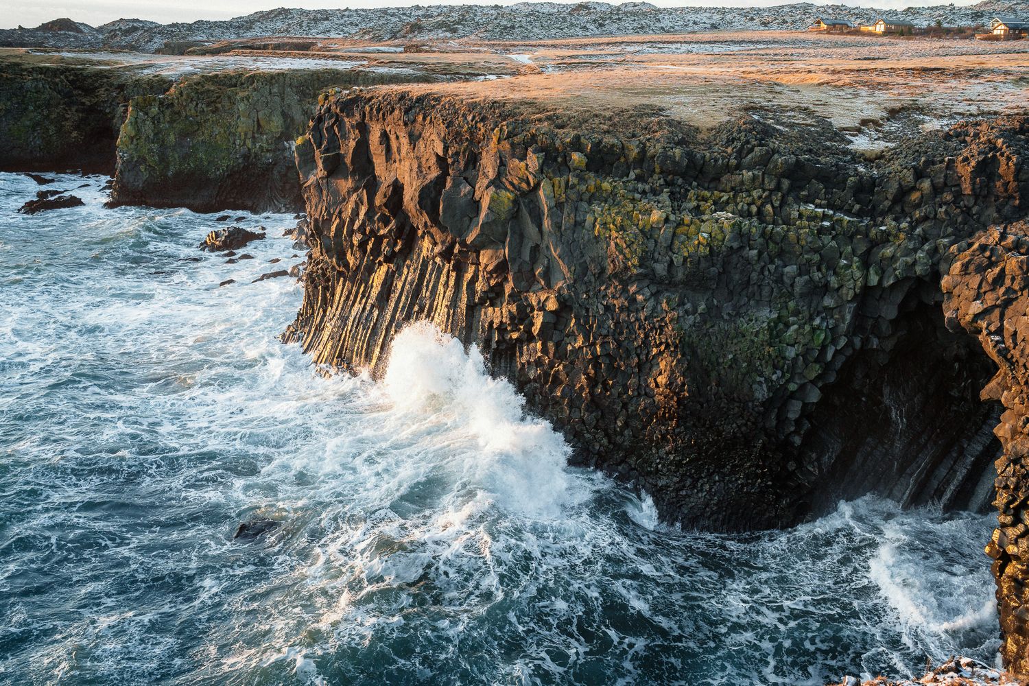 Luftaufnahme von Island: Morgensonne beleuchtet weite Moore und gefrorene Seen vor majestätischen, teils schneebedeckten Bergen.