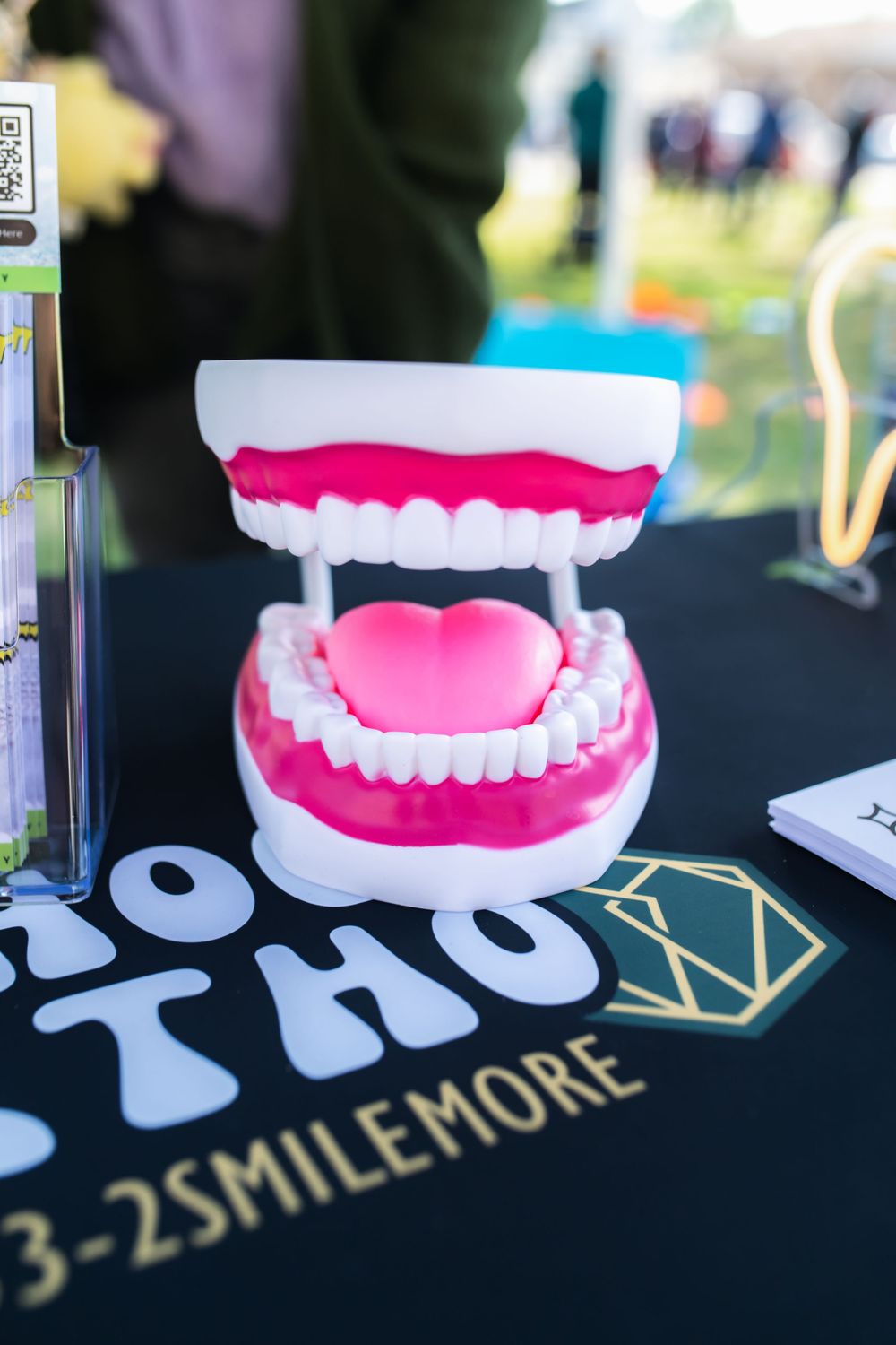 Large pink and white dental model jaw on a table at an orthodontic booth displaying the number 3-2SMILEMORE.