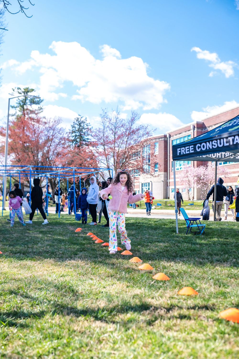 Young girl running through orange cone obstacle course at outdoor community event with free consultation tent.