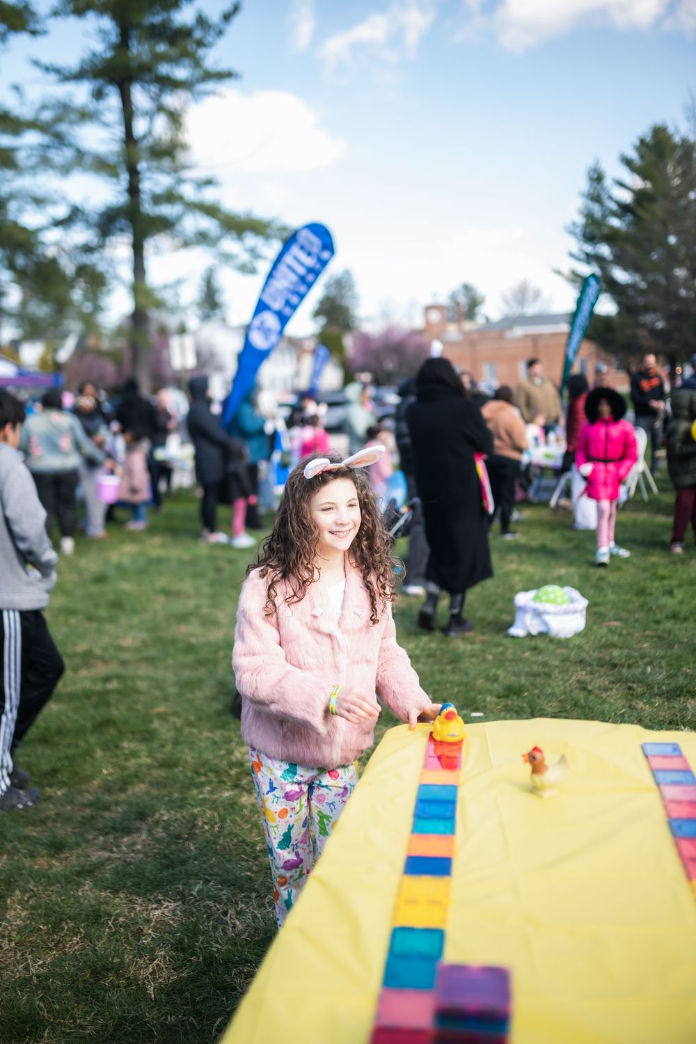 Young girl in pink fur jacket plays with colorful block game at outdoor spring festival event.