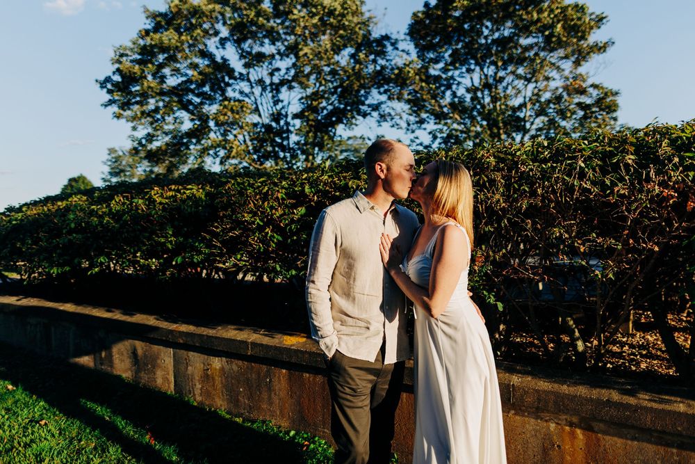 A couple shares a romantic moment at sunset in a garden setting with lush greenery in the background.