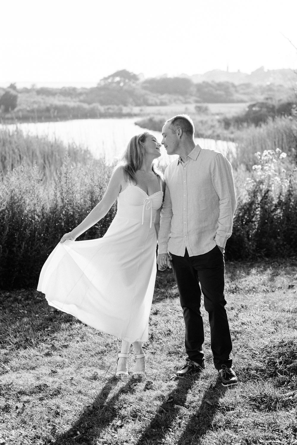 Black and white romantic sequence of a couple sharing tender moments in a sunlit meadow with tall grass and flowers.
