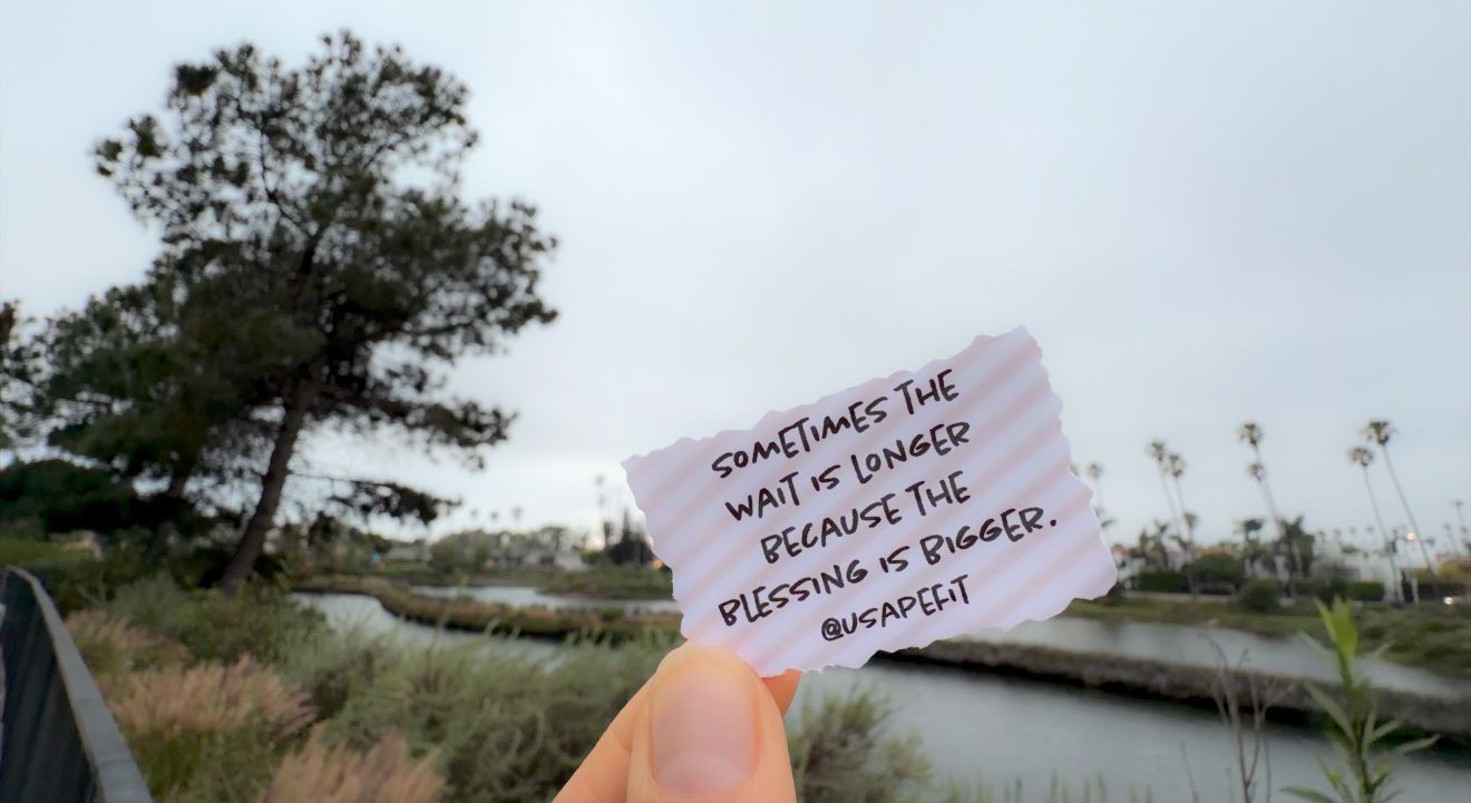 Hand holding a torn paper note with text against a scenic waterway and tree landscape background.
