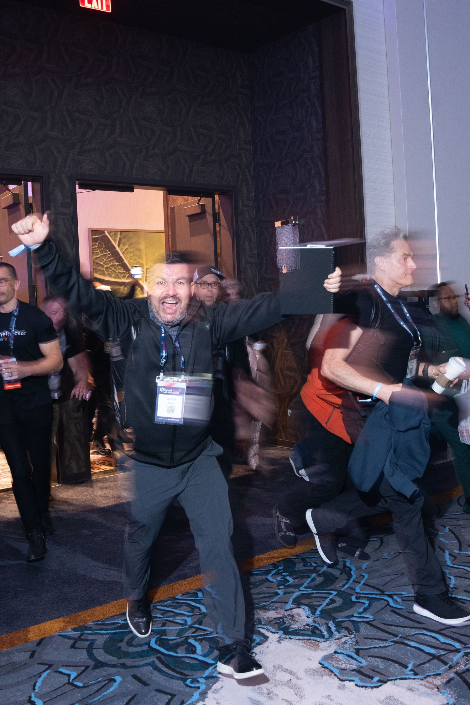 Excited man with badge raises fist at a crowded conference event, celebrating with attendees in a large venue.