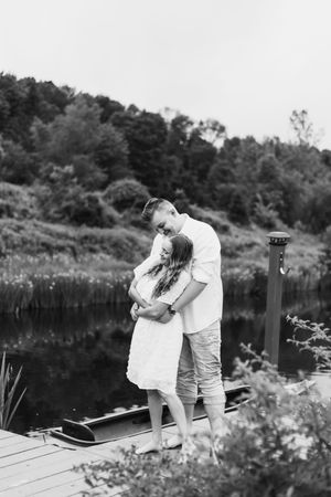 A romantic moment captured on a lakeside dock with white clothing against a natural backdrop.