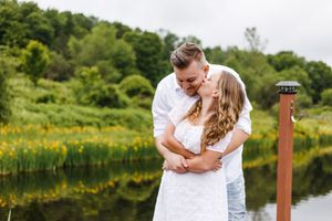 Romantic couple shares tender moments by a serene lake surrounded by lush greenery and wildflowers on a summer day.