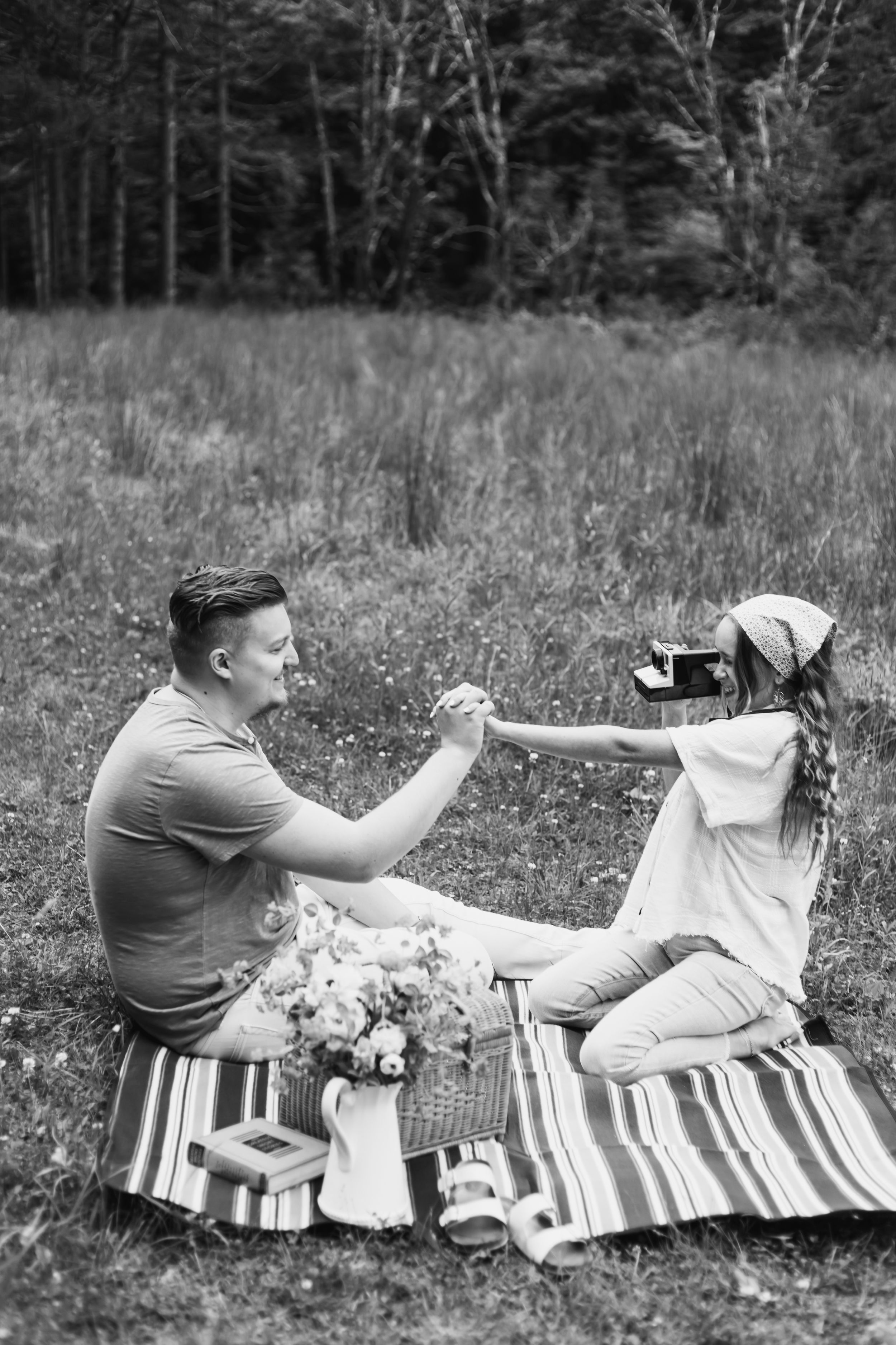 A sequence of black and white photos showing a couple having a playful moment on a striped blanket in a meadow.