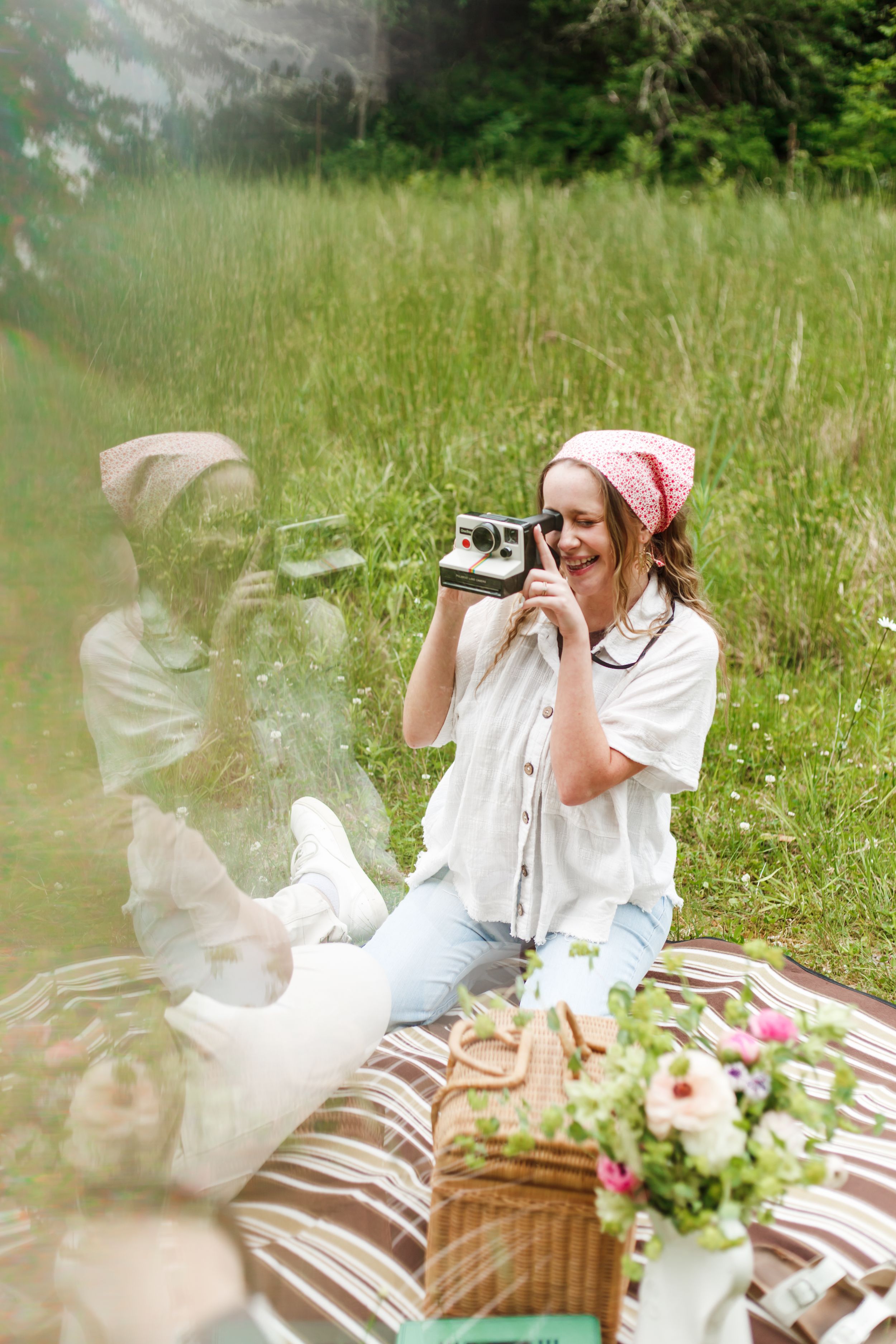A picnic setup in a sunny meadow with a wicker basket and white linens surrounded by flowers.