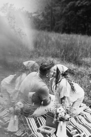 Black and white romantic picnic scene with couple laying on striped blanket in dreamy meadow setting.