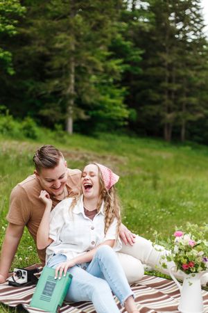 A joyful couple sharing laughter while having a picnic on a blanket in a green meadow.