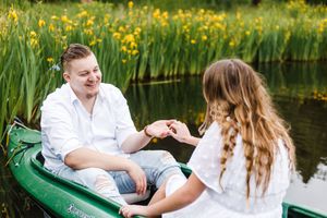 People share a romantic moment in a green canoe surrounded by yellow wildflowers and calm water.