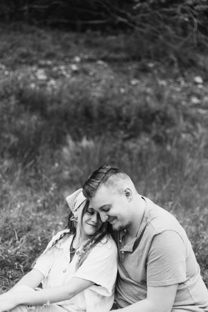 A tender moment between two people laying together on grass in black and white.