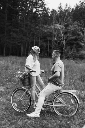 A couple shares a playful moment on a vintage tandem bicycle in a black and white countryside setting.