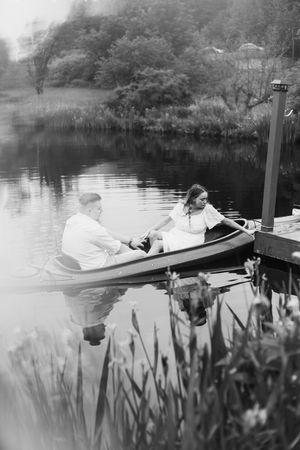 A romantic black and white scene of a couple canoeing on a tranquil lake beside a wooden dock.