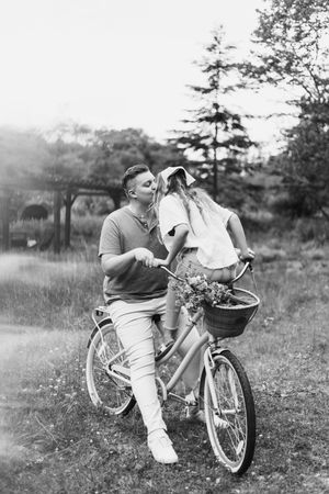 Black and white photo of couple with vintage bicycle and flower basket in meadow.