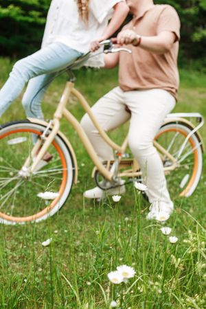 Close-up view of someone riding a vintage bicycle through grass with white daisies in the foreground.